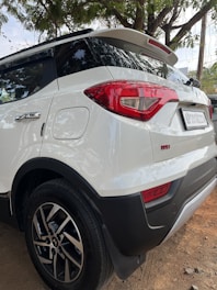 the rear end of a white suv parked on a dirt road