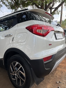 the rear end of a white suv parked on a dirt road