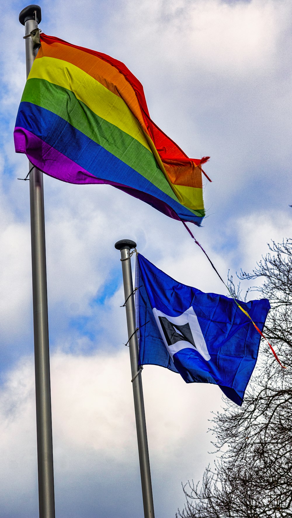 two rainbow flags flying in the wind on a cloudy day