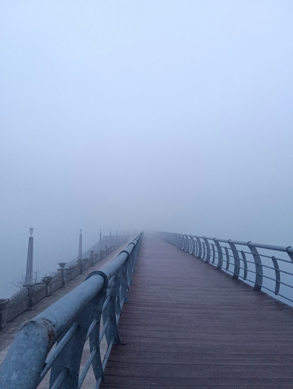a wooden bridge with a metal railing on a foggy day