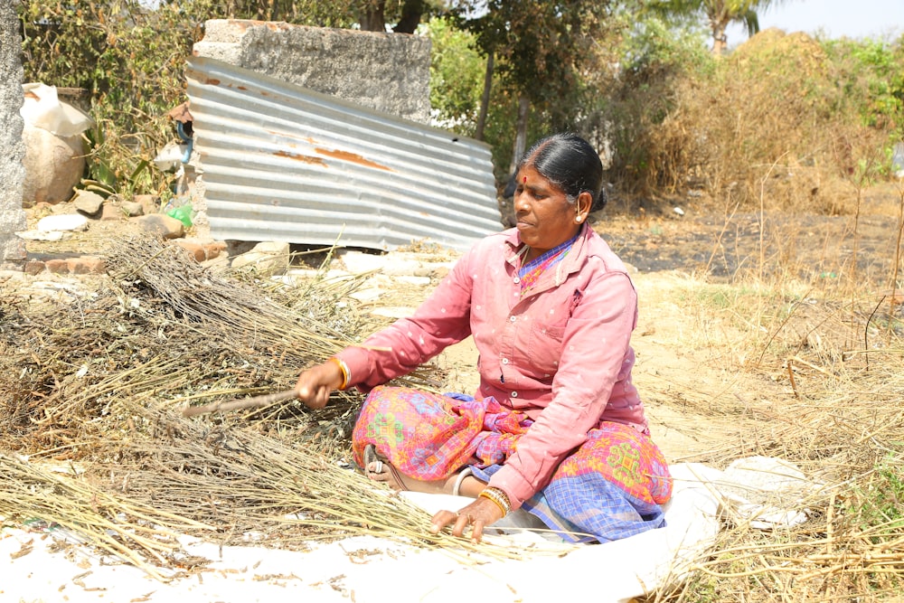 a woman sitting on the ground next to a pile of hay