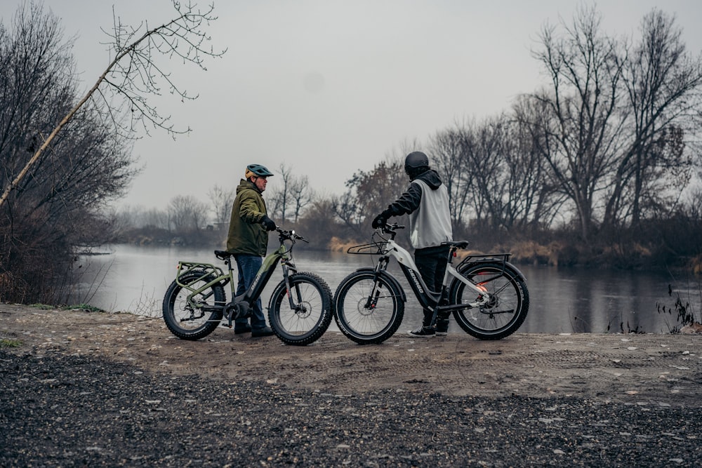 a couple of men standing next to bikes near a lake