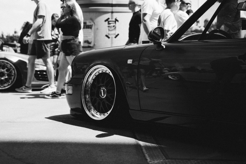 a group of people standing around a black car