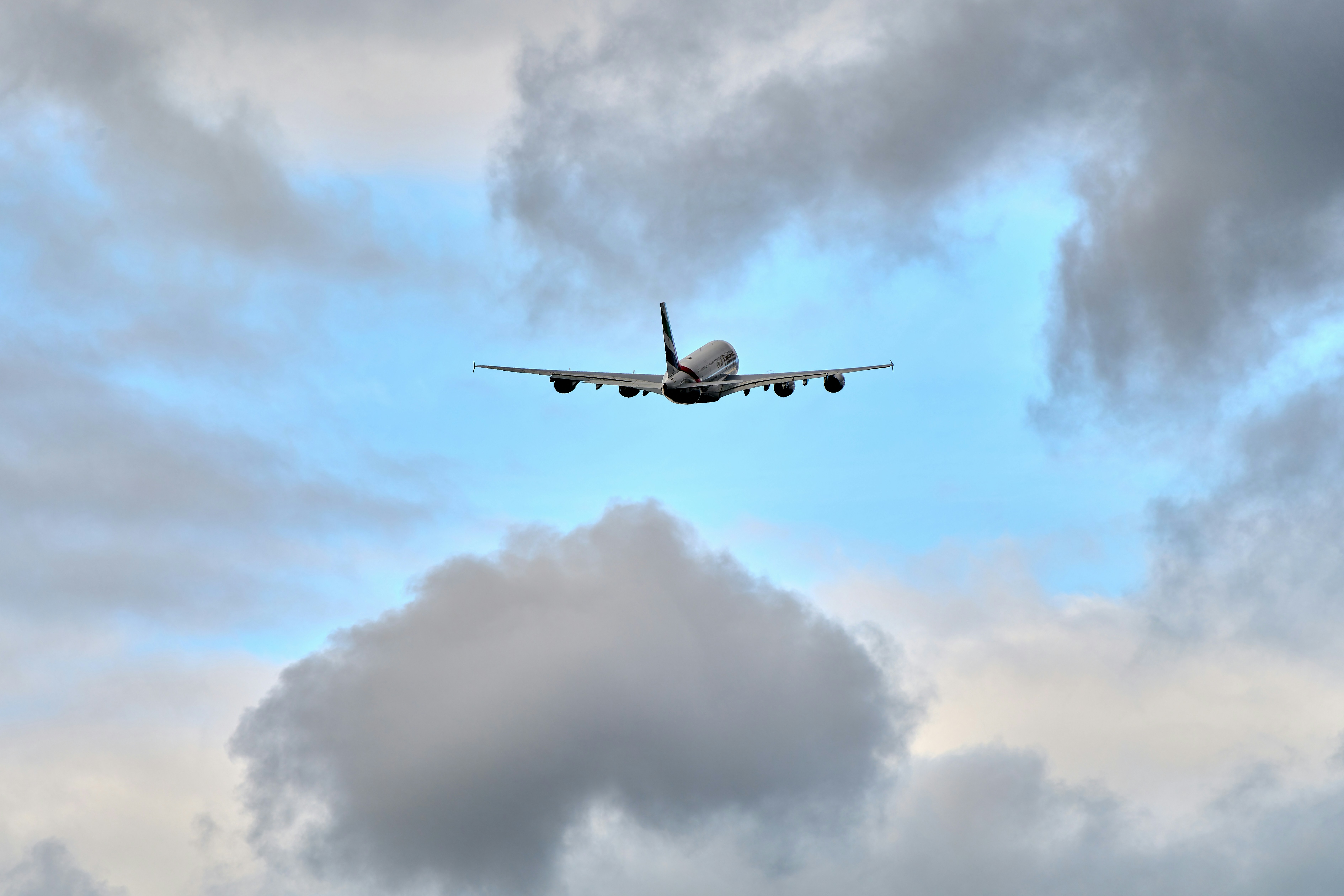an airplane flying through a cloudy blue sky, 