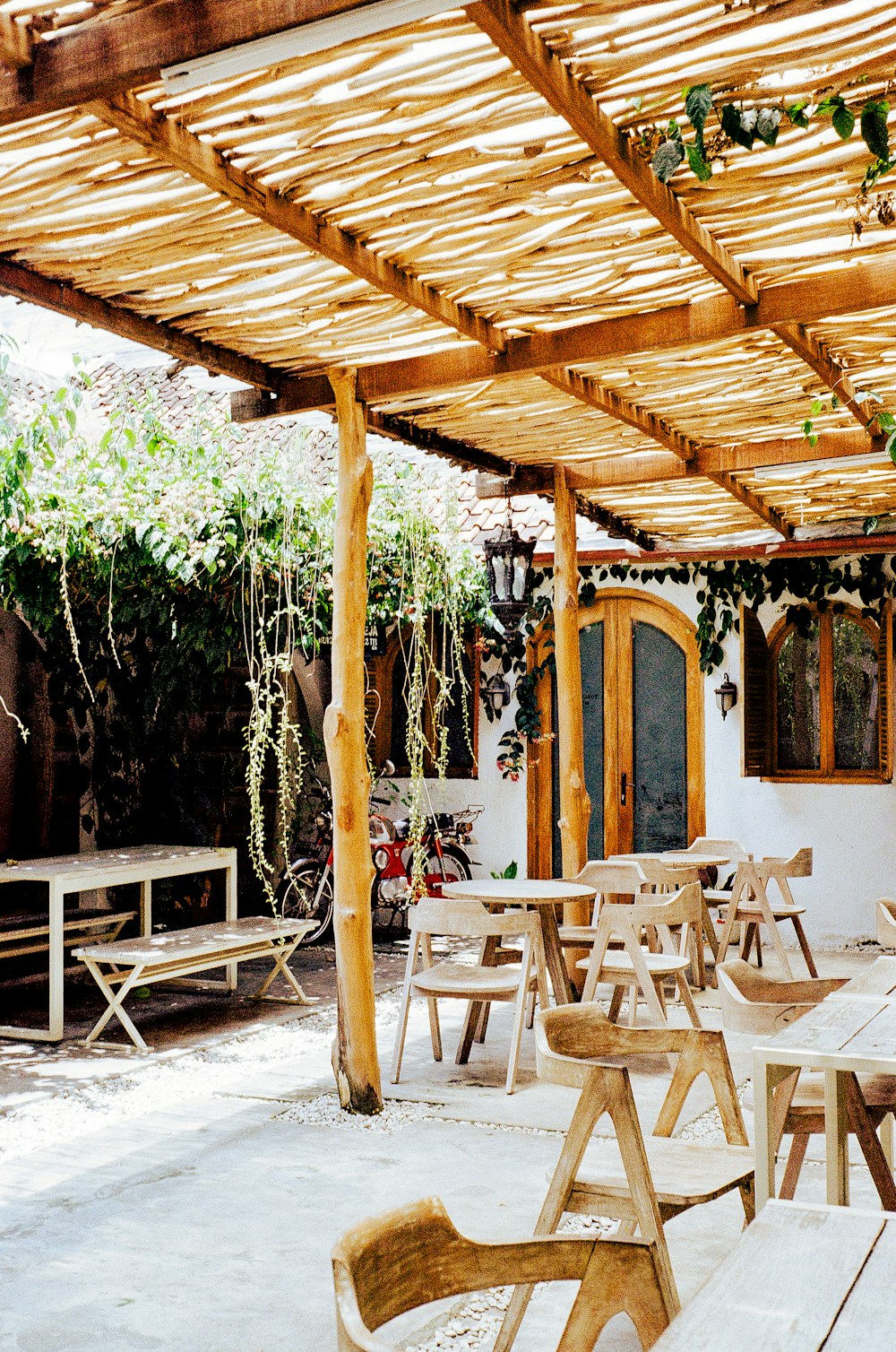 a patio with wooden tables and benches under a pergolated roof