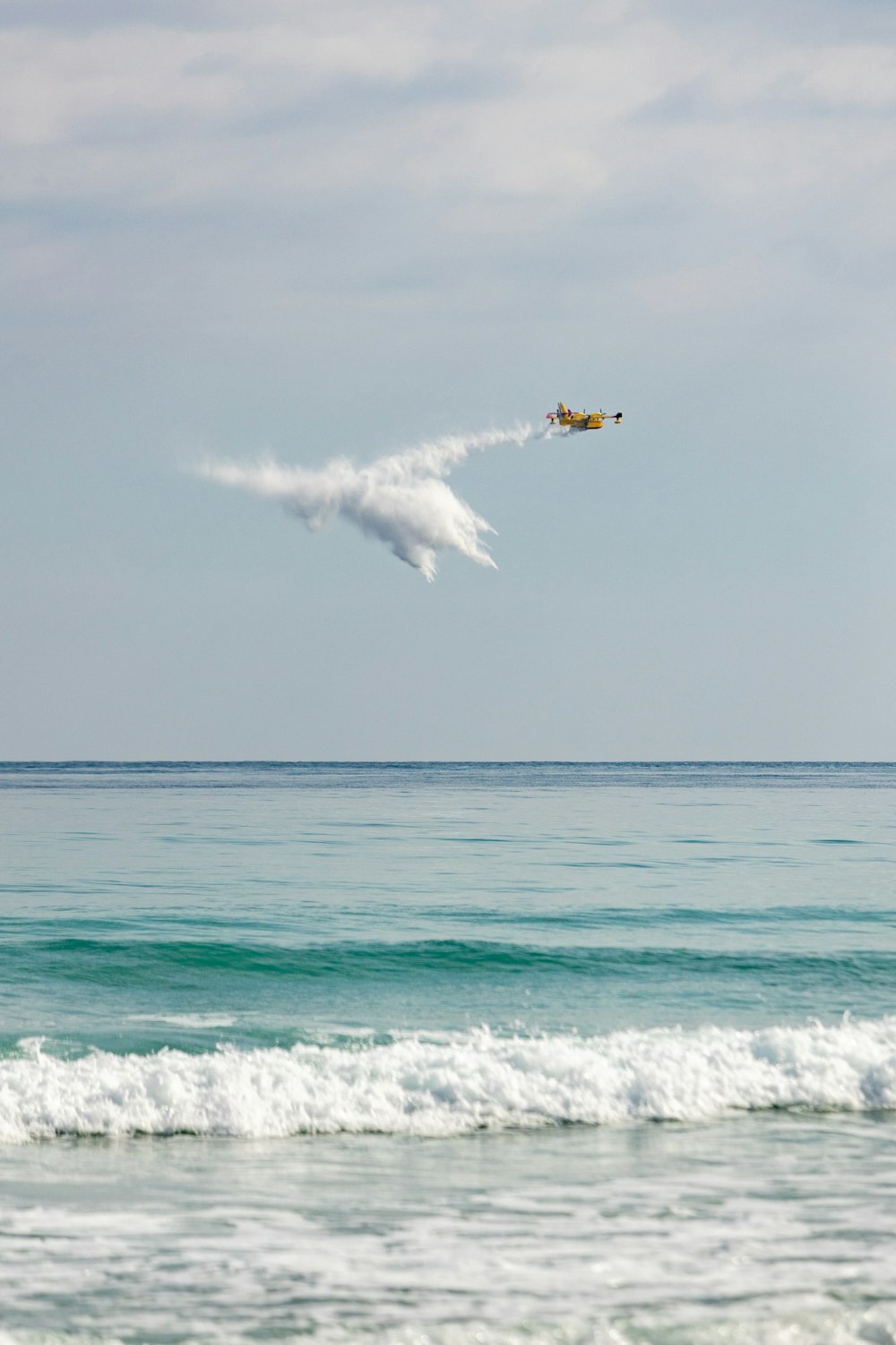 a plane flying over the ocean with a cloud in the sky