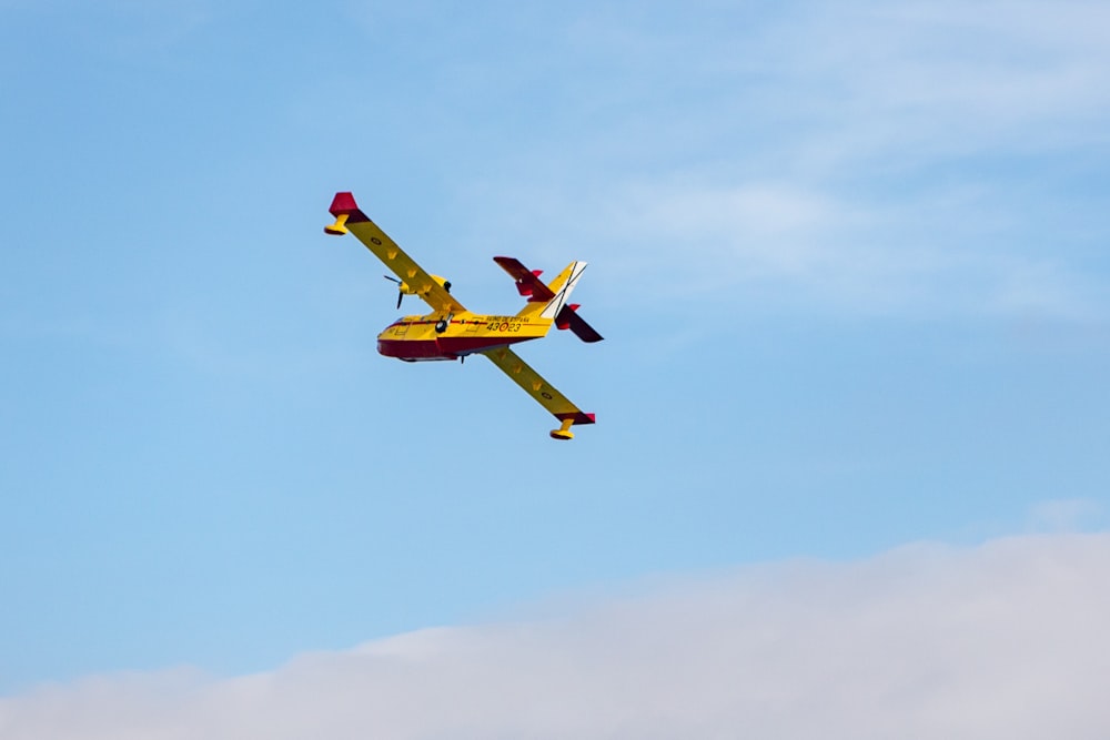 a yellow and red plane flying in the sky