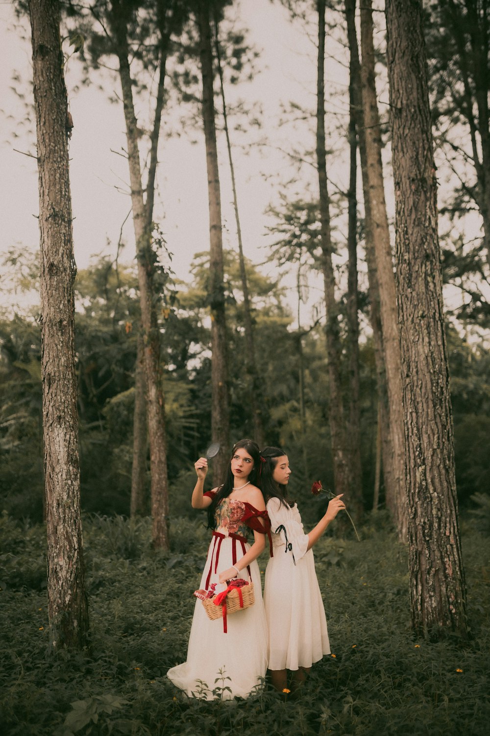 two women in white dresses standing in a forest