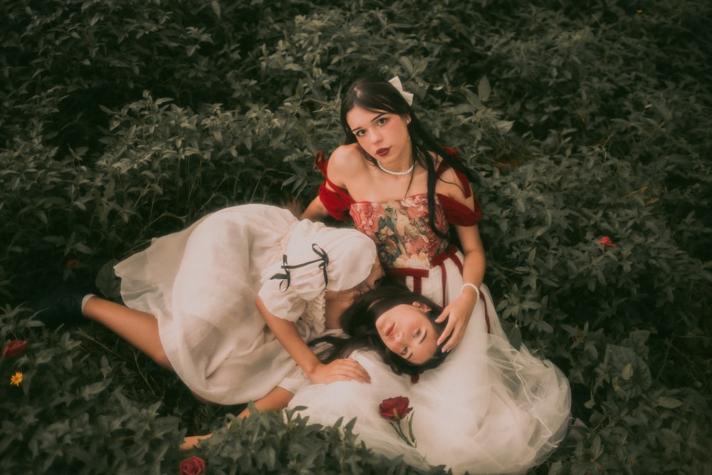 a couple of women laying on top of a lush green field