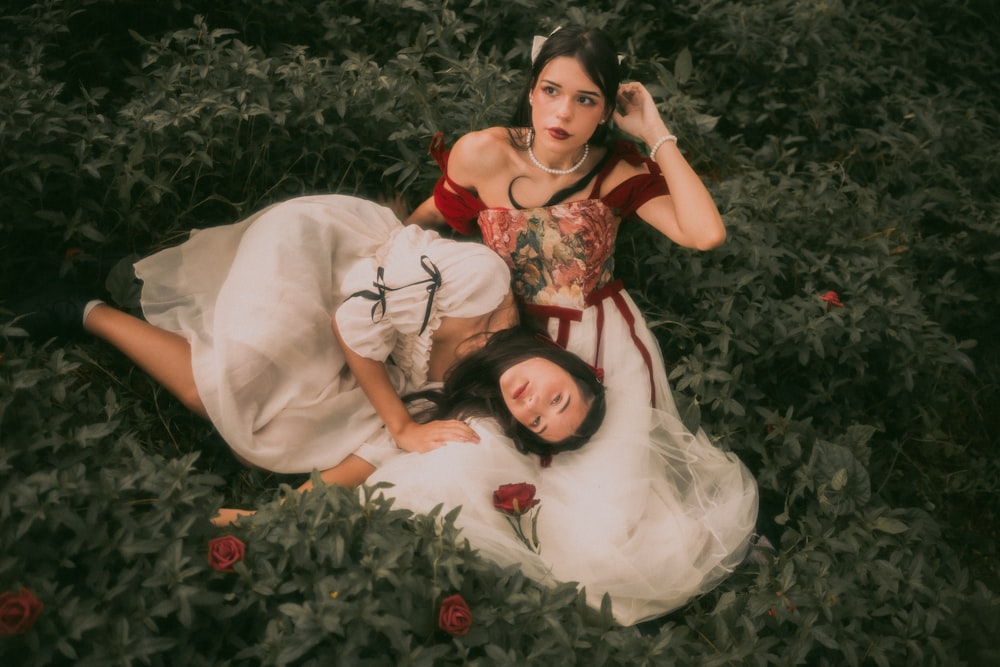 a couple of women laying on top of a lush green field