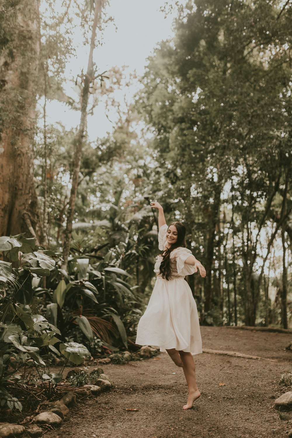 a woman in a white dress is dancing in the woods