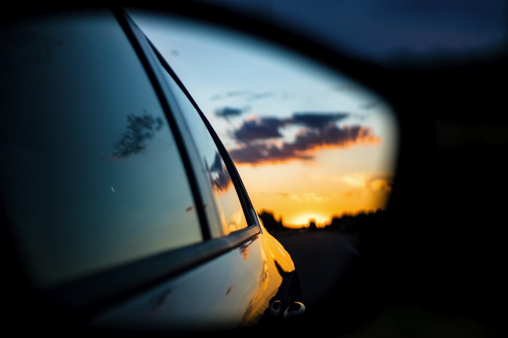 a car's side view mirror reflecting a sunset