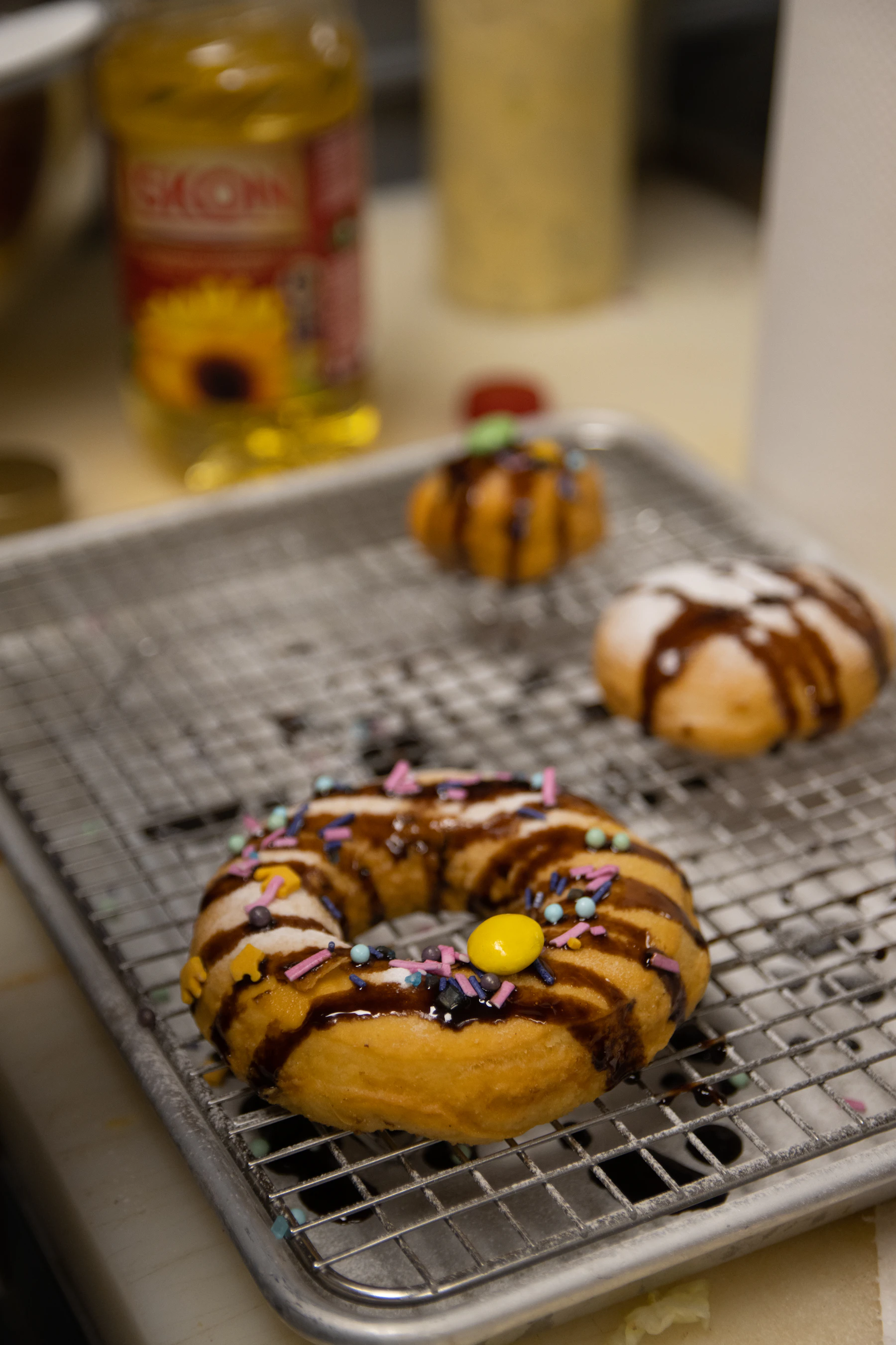 Homemade ring donuts with chocolate drizzle and sprinkles on a wire rack over a sheet pan