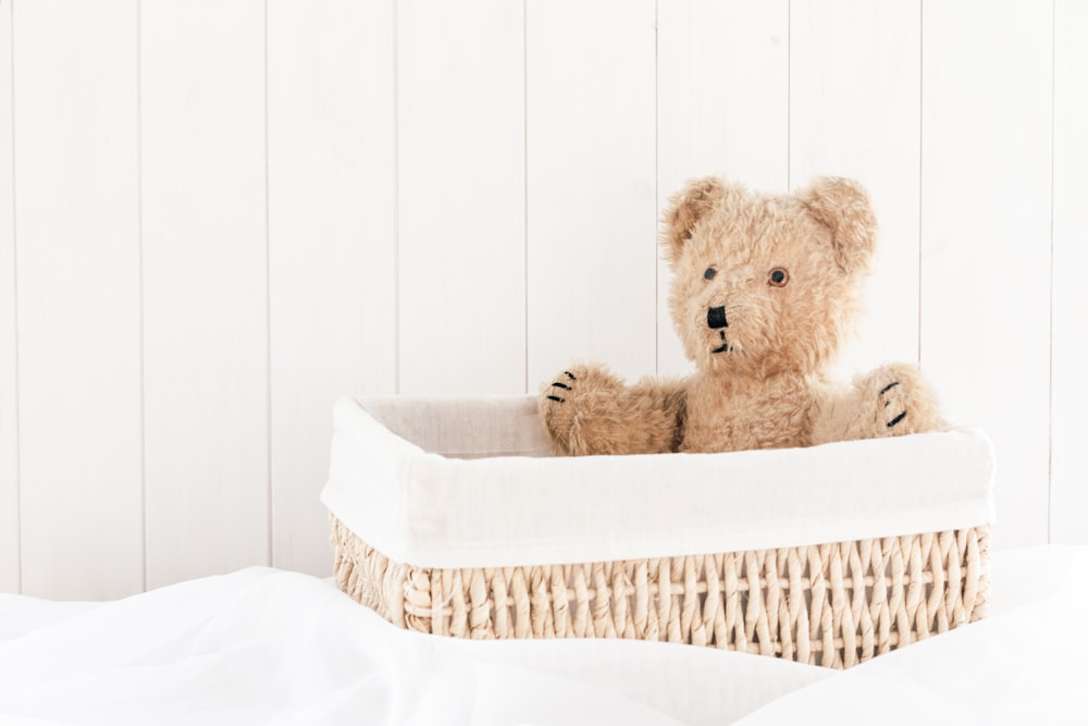 a teddy bear sitting in a basket on a bed