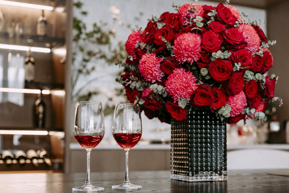 a vase of flowers and two wine glasses on a table
