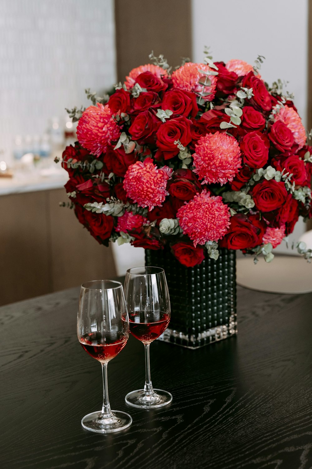 a vase of flowers and two wine glasses on a table