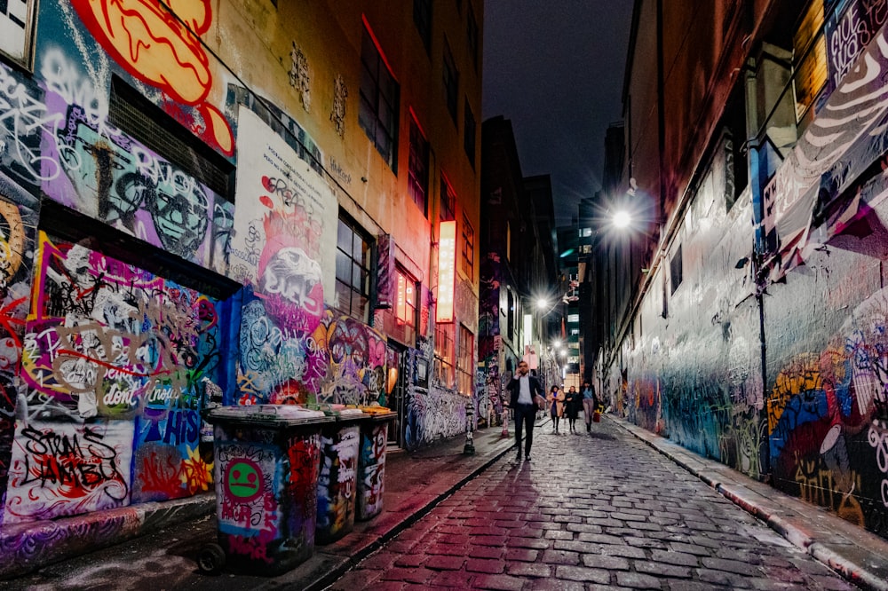 una persona caminando por una calle junto a una pared cubierta de grafitis