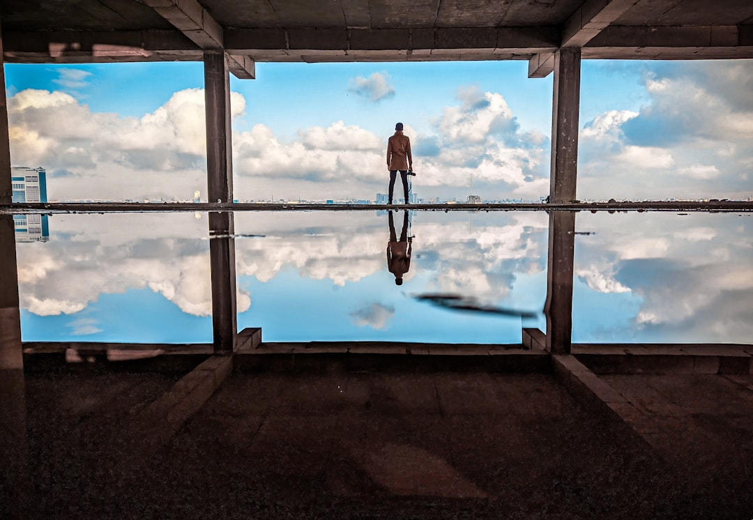 a man standing in front of a large window, Lonely man standing on a building with a water reflection