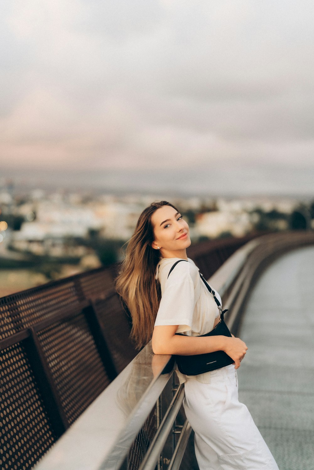 a woman leaning on a fence with a city in the background