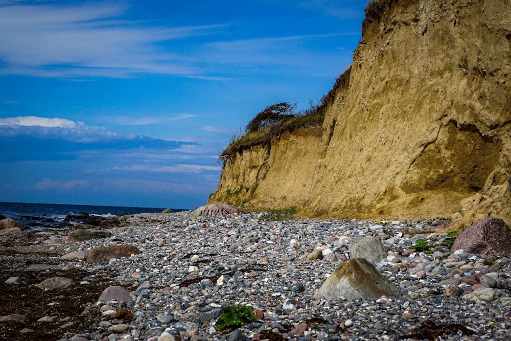 a rocky beach next to a cliff under a blue sky