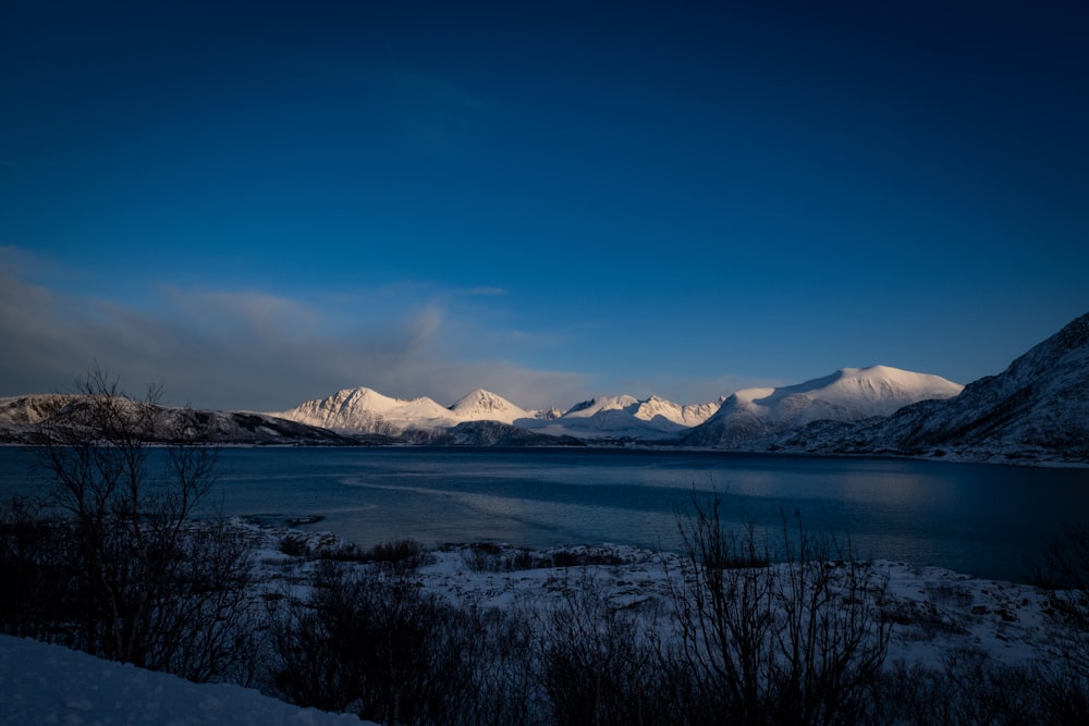 a lake surrounded by snow covered mountains under a blue sky