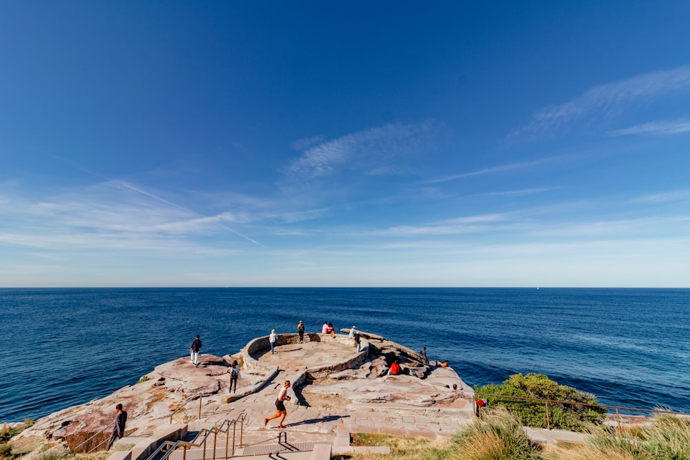 a group of people standing on top of a cliff next to the ocean