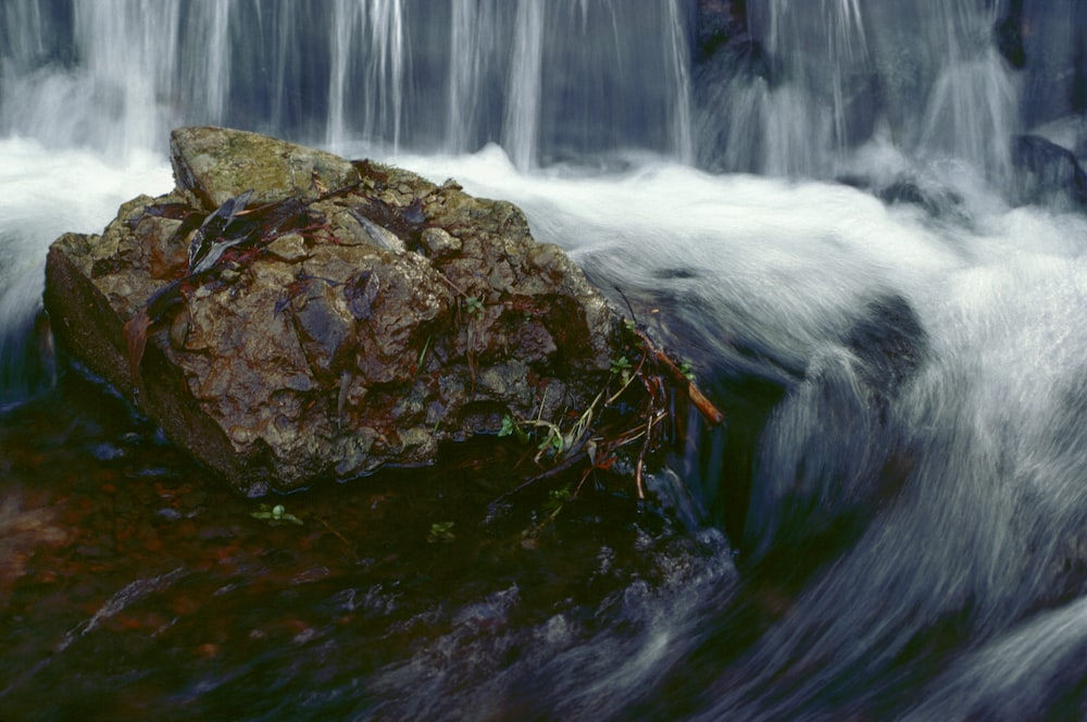 a rock sitting on top of a river next to a waterfall