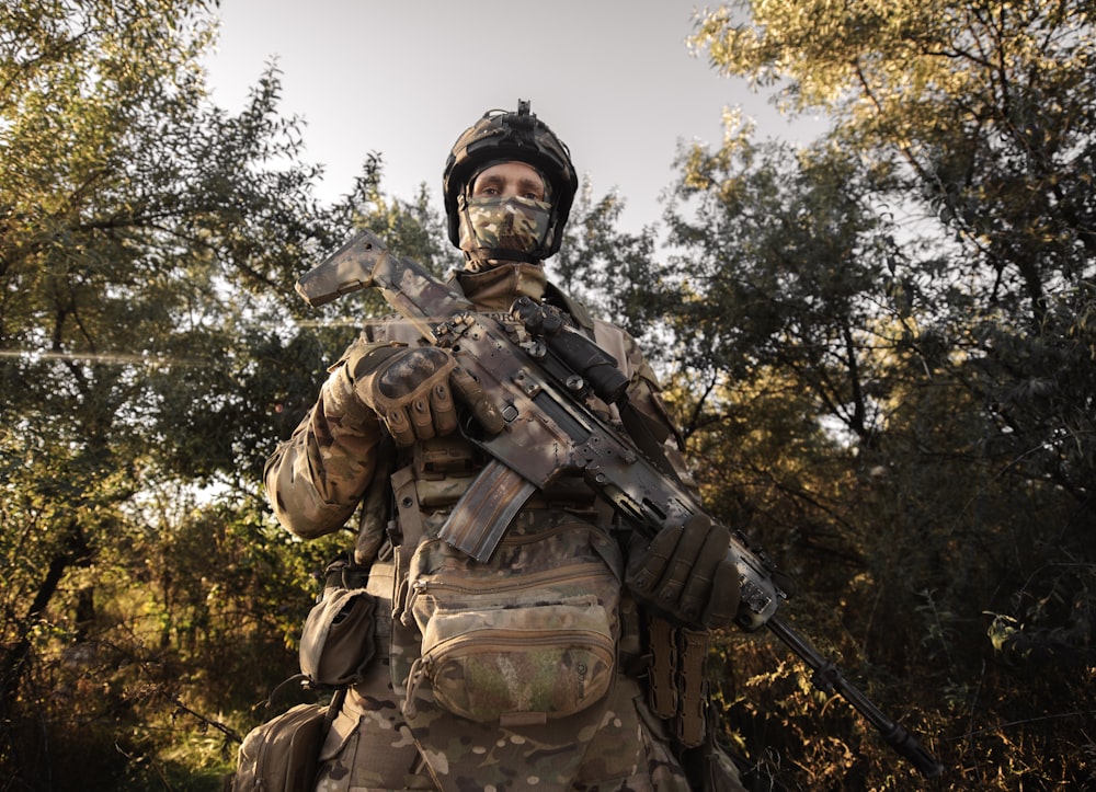 a man in camouflage holding a rifle in a wooded area