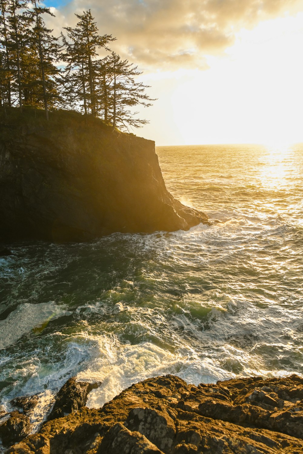 the sun is setting over the ocean and a rocky shore