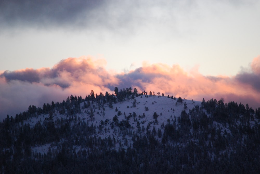 a mountain covered in snow and clouds at sunset
