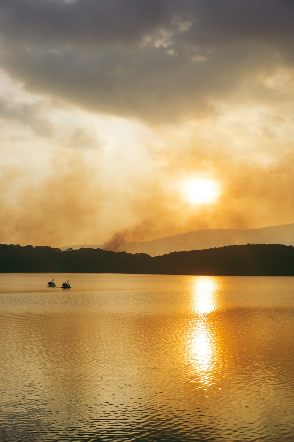 a couple of boats floating on top of a lake under a cloudy sky