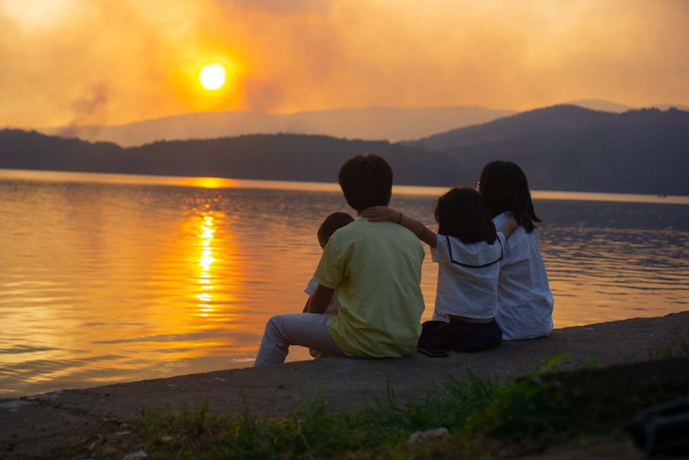 a couple of kids sitting next to a body of water