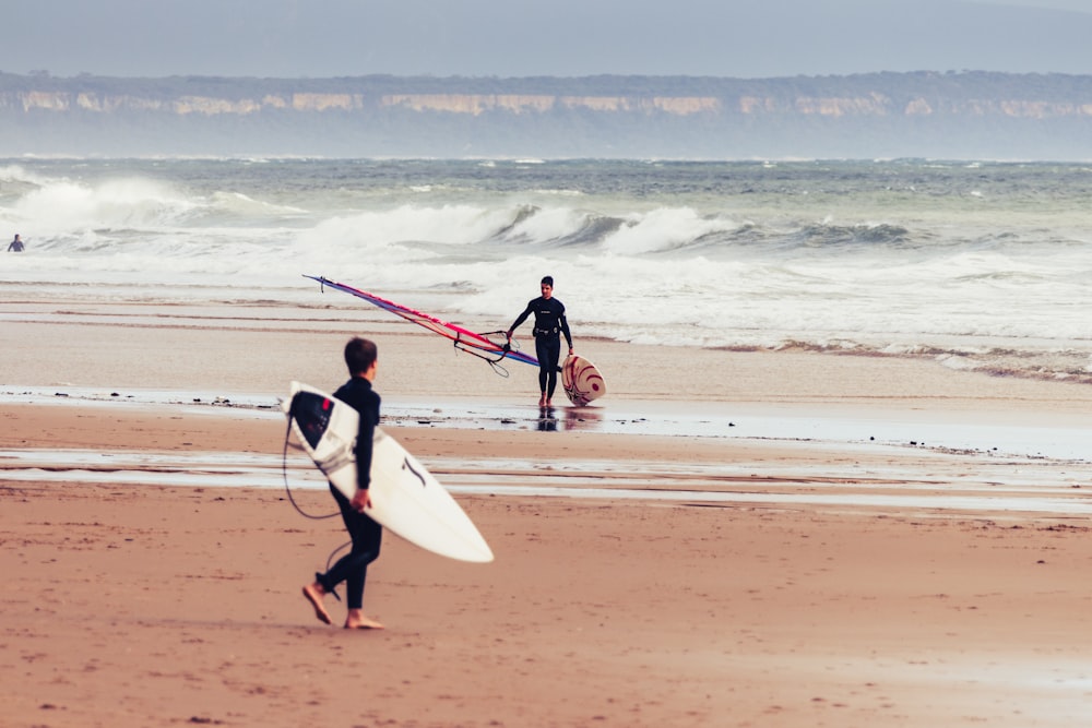 a couple of men walking across a beach holding surfboards