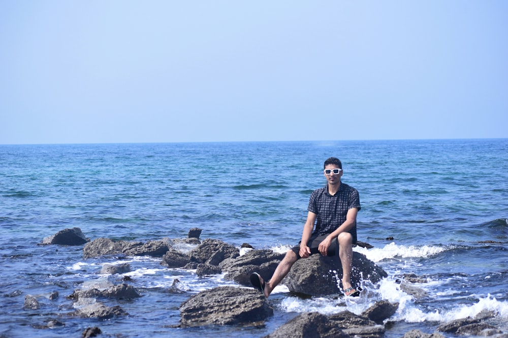 a man sitting on top of a rock near the ocean