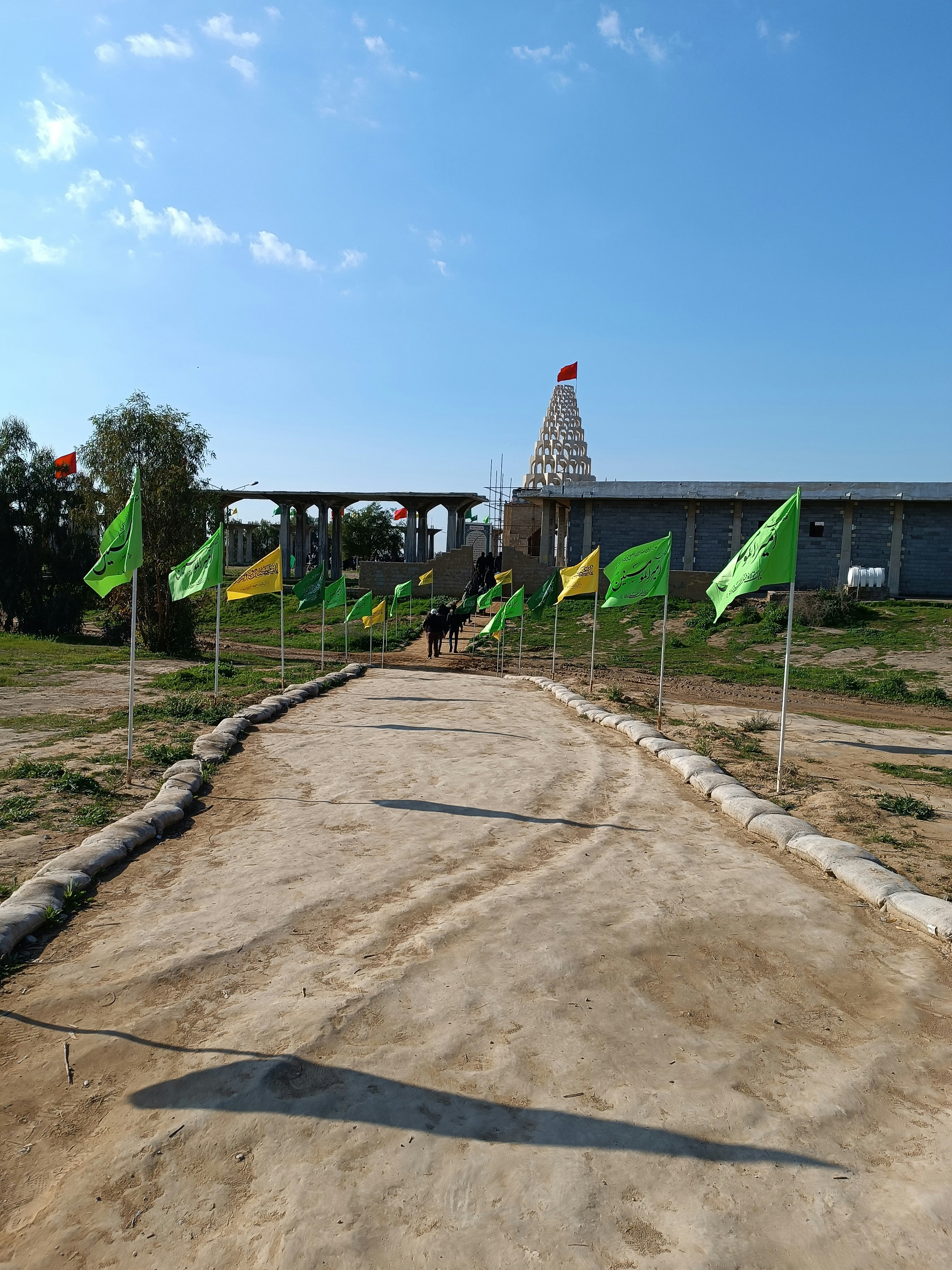 a dirt road with flags and a building in the background