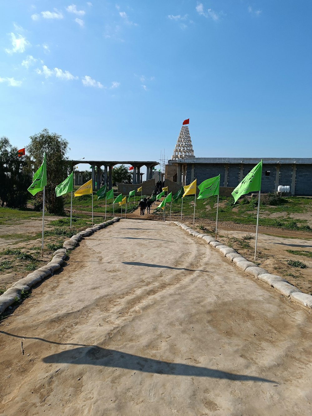 a dirt road with flags and a building in the background