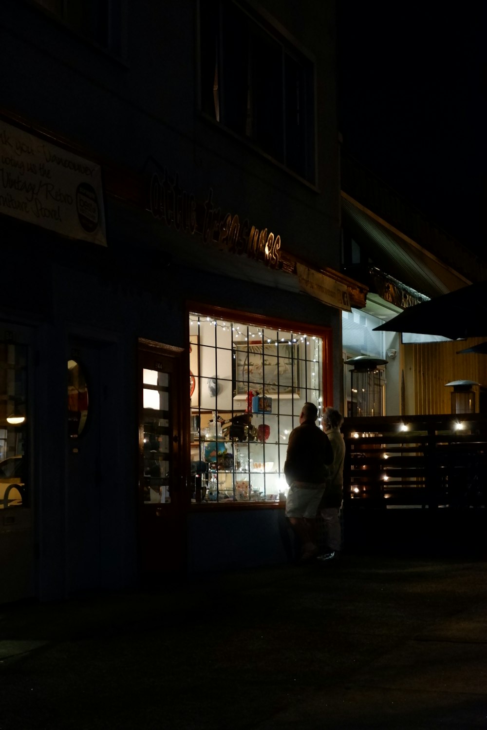 a couple of people standing outside of a store at night