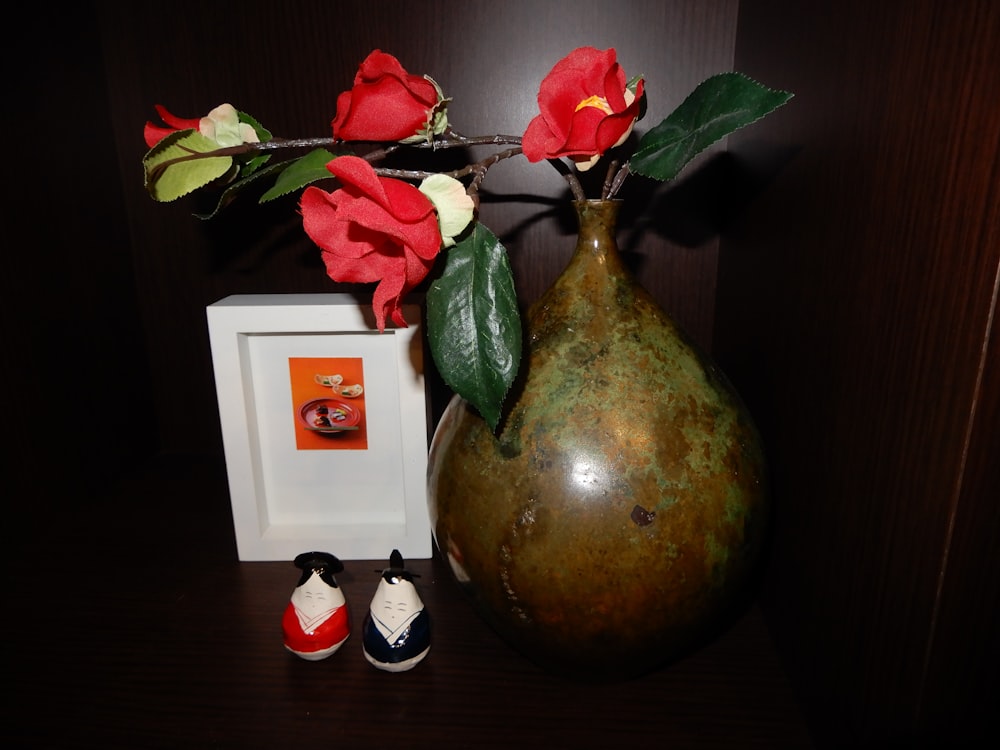 a vase with red flowers and a pair of baby shoes