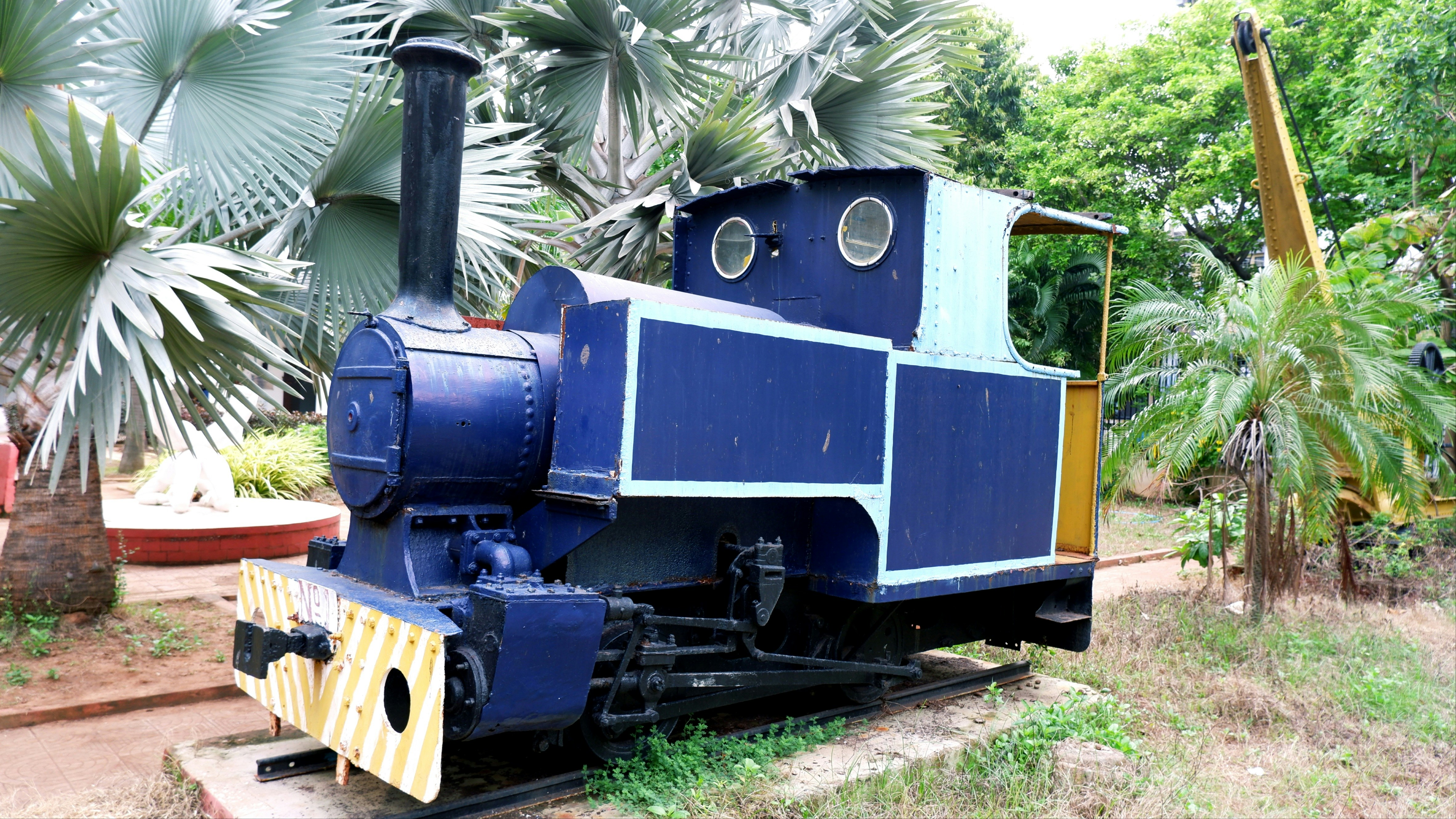 a blue and yellow train sitting on top of a train track, 18th Century Toy Train Steam Engine Locomotive built by British now preserved in Visakha Museum on RK Beach Road, Visakhapatnam
