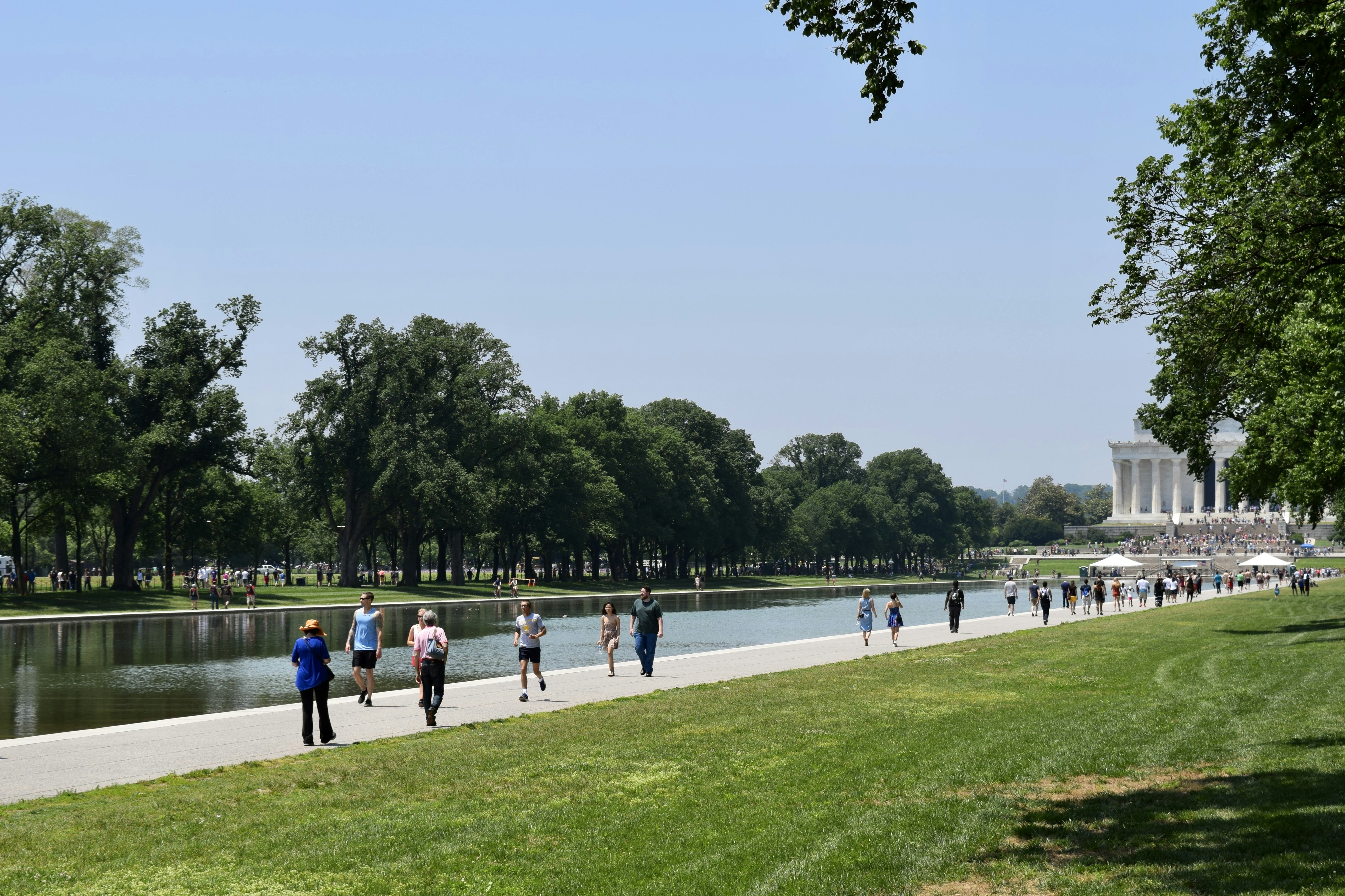 a group of people walking down a sidewalk next to a lake