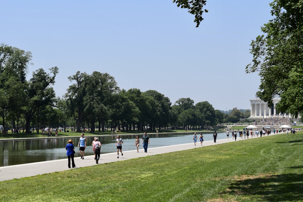 a group of people walking down a sidewalk next to a lake