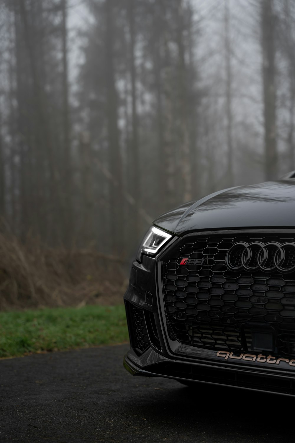 the front end of a black car parked on a road