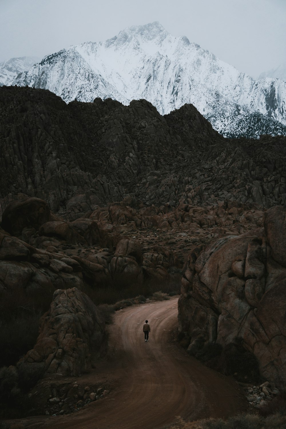 a person walking down a dirt road in front of a mountain