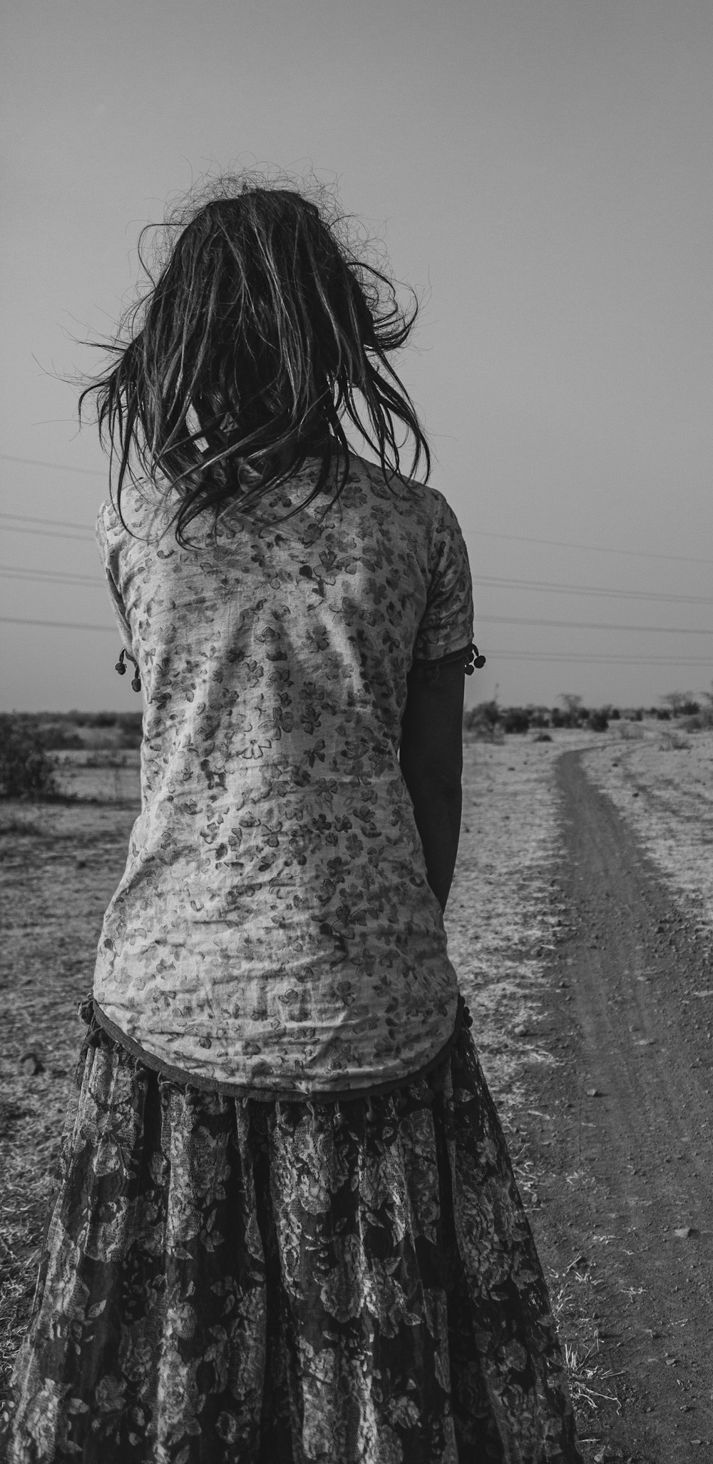 a woman walking down a dirt road next to a field