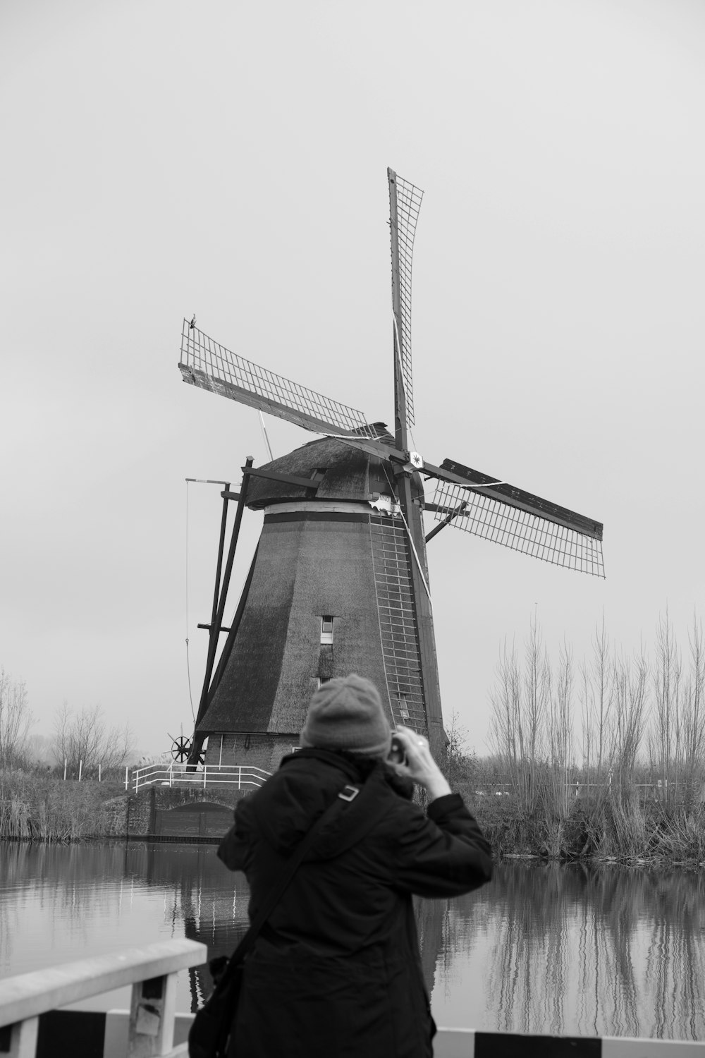 a black and white photo of a person taking a picture of a windmill