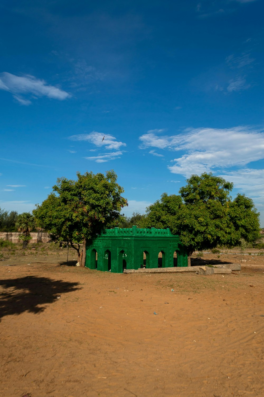 a green building sitting in the middle of a dirt field