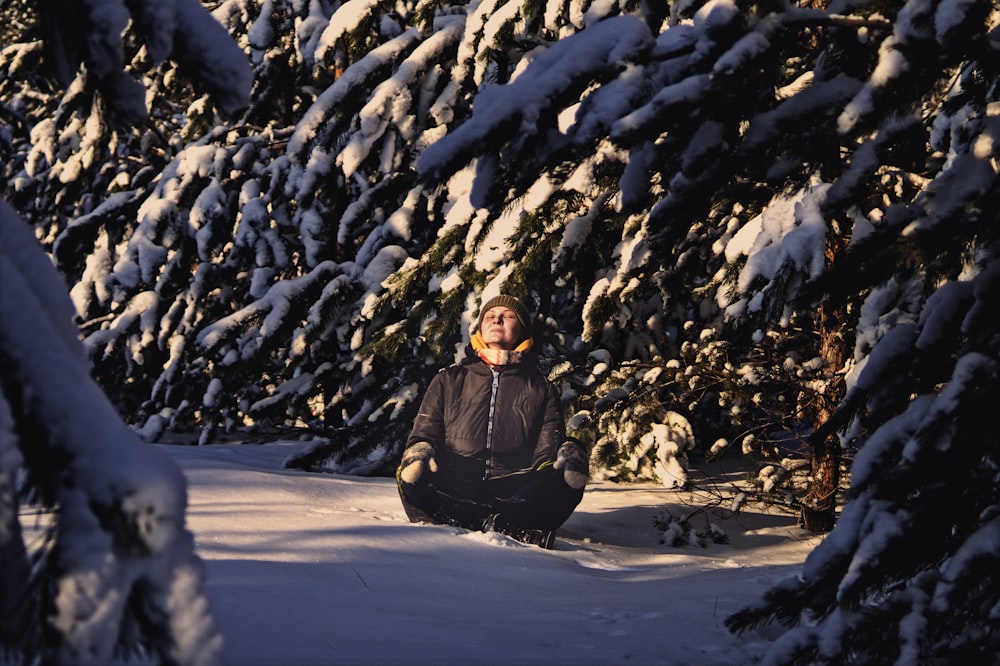 a person sitting in the snow in front of a tree