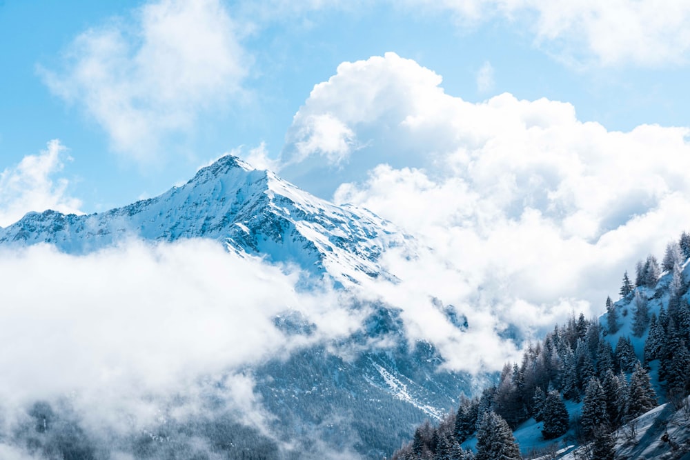 a mountain covered in snow and clouds under a blue sky