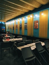 a dining area with tables and chairs in front of a yellow and blue wall