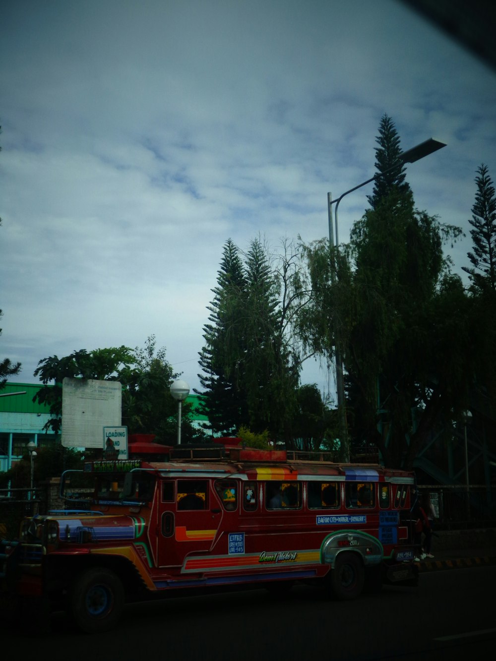 a red bus driving down a street next to a forest